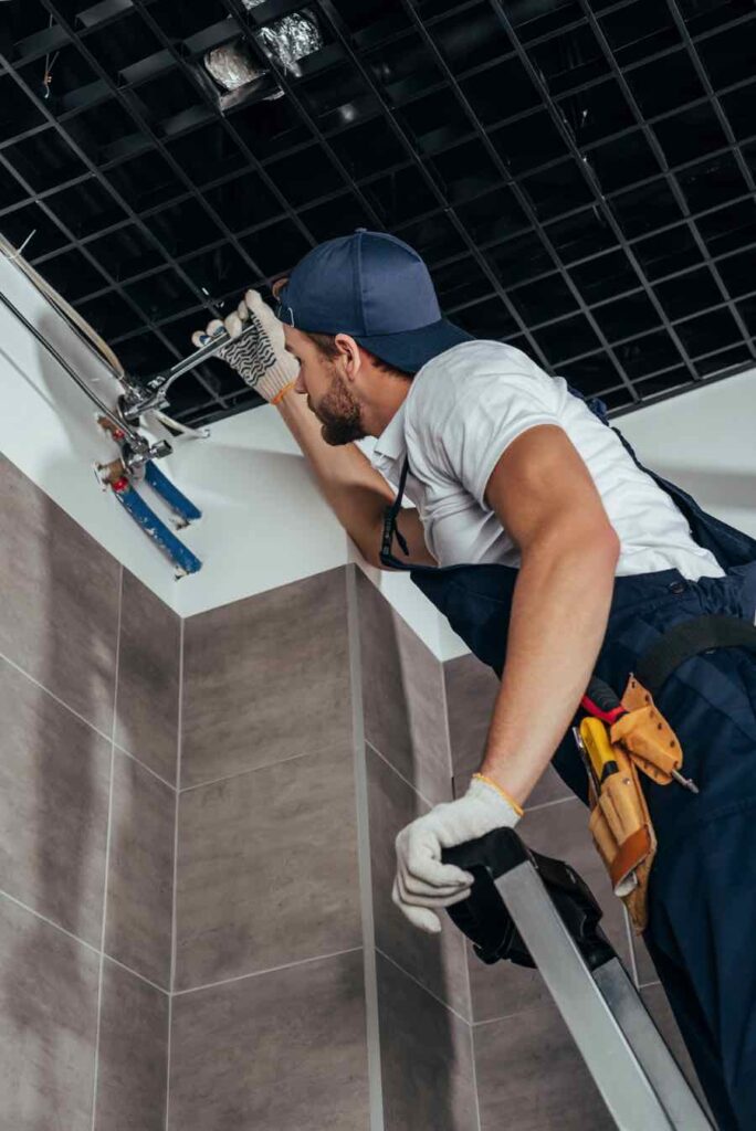 low-angle-view-of-plumber-standing-on-ladder-and-w-N9D4T8S.jpg