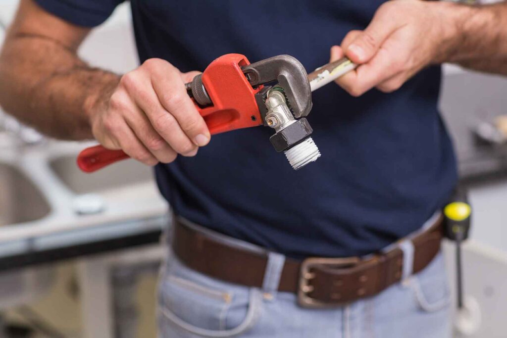 plumber-fixing-pipe-with-wrench-in-the-kitchen-PW55SHB.jpg